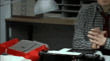 a man in a plaid shirt and tie is talking to another man in front of a box that says odds