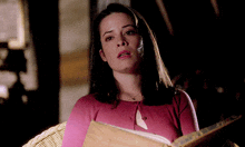 a woman in a pink sweater is sitting in a chair reading a book