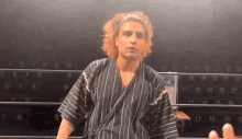 a man with curly hair is standing in a boxing ring wearing a striped robe .
