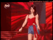 a woman in a red top and blue shorts is on a stage