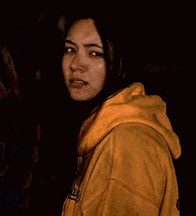 a woman in a yellow hoodie is looking at the camera .