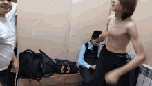 a boy without a shirt sits on a bench next to a black bag that says ' headphones ' on it