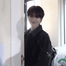a young man in a black jacket is peeking out of a doorway .