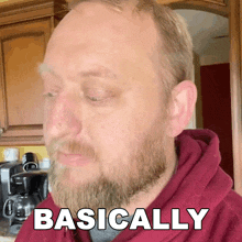 a man with a beard is wearing a red hoodie and the word basically is on his face