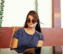 a woman wearing sunglasses and a blue shirt is sitting at a table