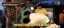 a group of people are standing around a man who is laying on the ground with the words what 's happening written above him .