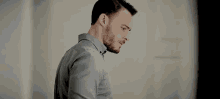 a man with a beard wearing a grey shirt is standing in a room .