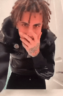 a man with dreadlocks is covering his mouth with his hands