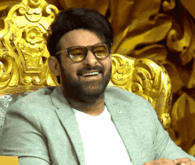a man with glasses and a beard is smiling in front of a gold chair