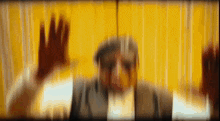 a blurry picture of a man behind a yellow curtain with his hands up .