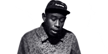 a black and white photo of a man wearing a supreme hat and a bow tie .
