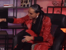 a woman in a red leather jacket is sitting in a chair and making a funny face .