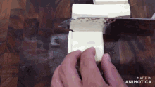 a person is cutting tofu with a knife on a wooden cutting board made by animatica