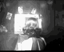 a black and white photo of a woman in a dark room looking at a television .