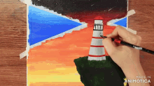 a person is painting a lighthouse on a piece of paper that says made in animatica on the bottom