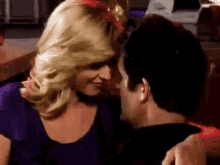 a man and a woman are kissing in a room . the woman is wearing a wig .