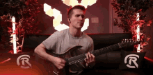 a man playing a guitar in front of a sign that says r on it