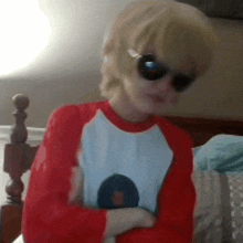 a person wearing sunglasses and a red shirt sitting on a bed