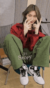 a woman wearing a red jacket and green pants is sitting on a chair with the word story on the back