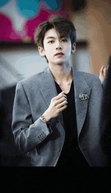 a young man wearing a grey jacket and a black shirt has a brooch that says rtx on it