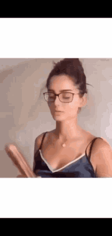 a woman wearing glasses and a blue tank top is holding a piece of paper in her hand .