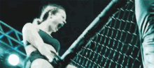 a woman is standing in a boxing ring with a chain link fence in the background .