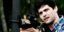 a man in a plaid shirt is holding a gun and saying " fuck " .
