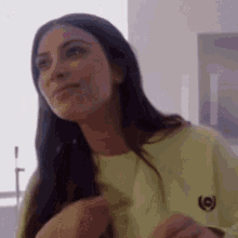 a woman with long hair is wearing a yellow shirt and smiling while standing in front of a window .