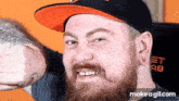 a man with a beard is wearing a hat and giving a thumbs up .