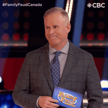 a man in a suit and tie holding a family feud canada sign