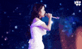 a woman in a white dress is singing into a microphone on a stage