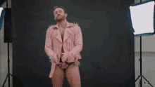 a man in a pink jacket and fishnet stockings stands in front of a black background with the letters kj on it