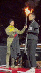 a man holding a torch stands next to a woman holding a jacket