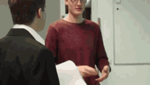 a man in a suit is holding a piece of paper and talking to another man .