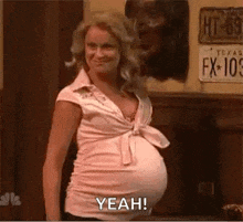 a pregnant woman in a pink shirt is standing in front of a wall .