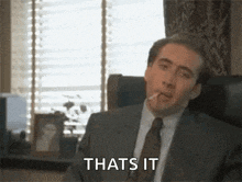 a man in a suit and tie is sitting in a chair smoking a cigarette and saying `` that 's it '' .