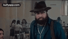 a man with a beard and glasses is wearing a hat and carrying a bag .