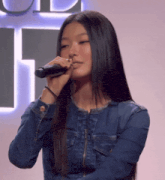 a woman singing into a microphone in front of a sign that says t.