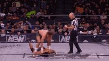 a wrestler is laying on the ground while a referee looks on during a aew wrestling match