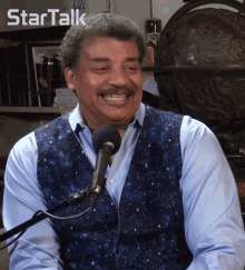 a man in a blue vest is smiling in front of a microphone with the words startalk above him