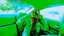 a person in a green jacket with a red flower on their head is sitting in a car