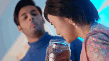 a man and woman are looking at a jar of chocolates