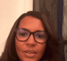 a woman wearing glasses is looking at the camera with a serious look on her face .