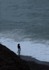a woman in a white skirt is standing on the shore of a body of water