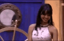 a woman in a white top is smiling in front of a ship wheel .