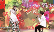 a man sitting next to a woman singing into a microphone in front of hearts