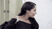 a woman with long dark hair is wearing a black off the shoulder top and holding a purse .