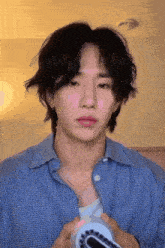 a young man with long black hair is wearing a blue plaid shirt and holding a camera .