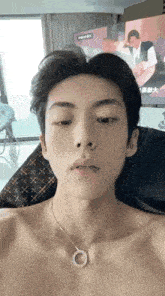 a shirtless young man wearing a necklace is sitting in a chair .