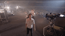 a man in a white shirt stands on a stage in front of a crowd that is watching a band